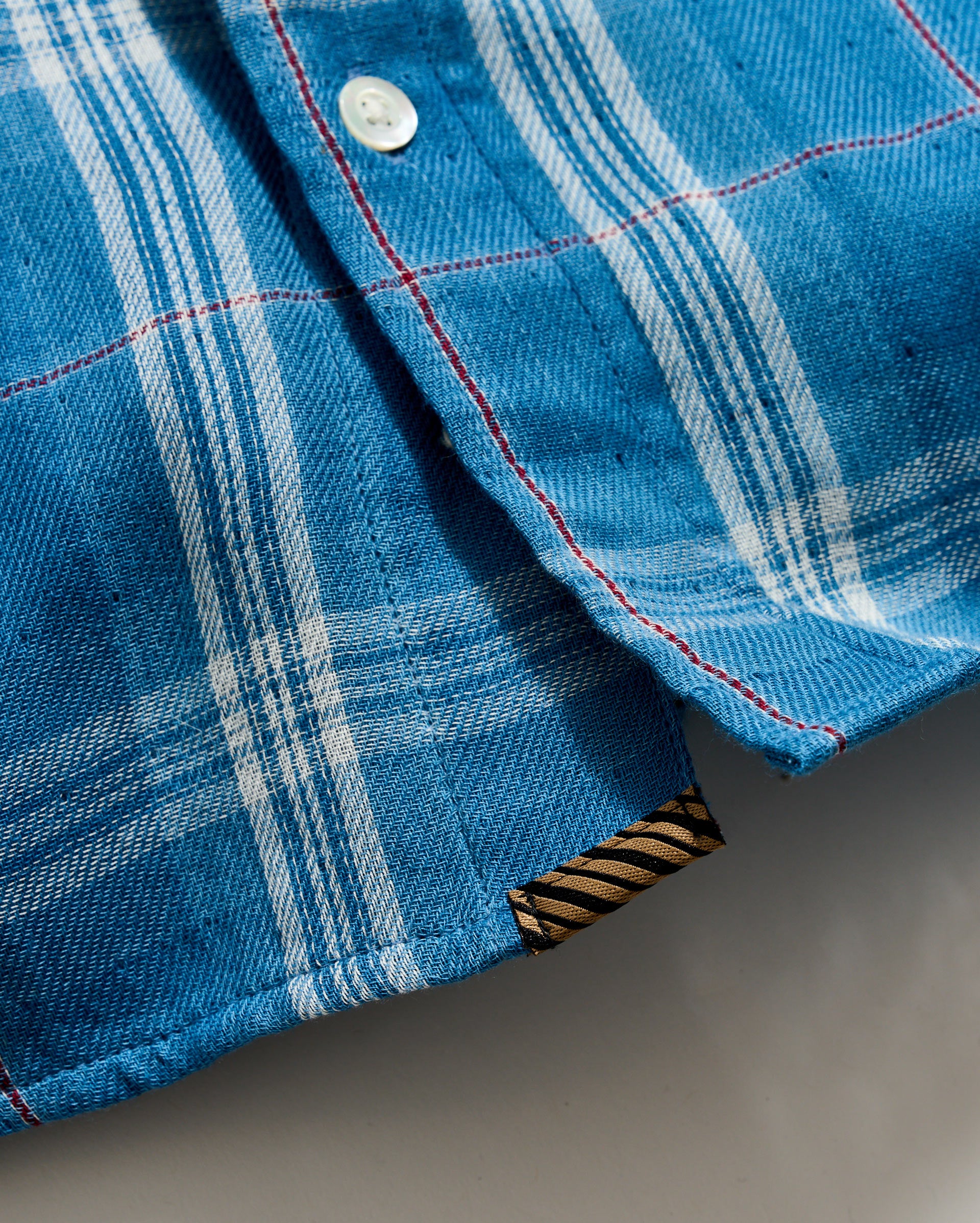 Close-up of a blue plaid fabric with a button and striped trim.