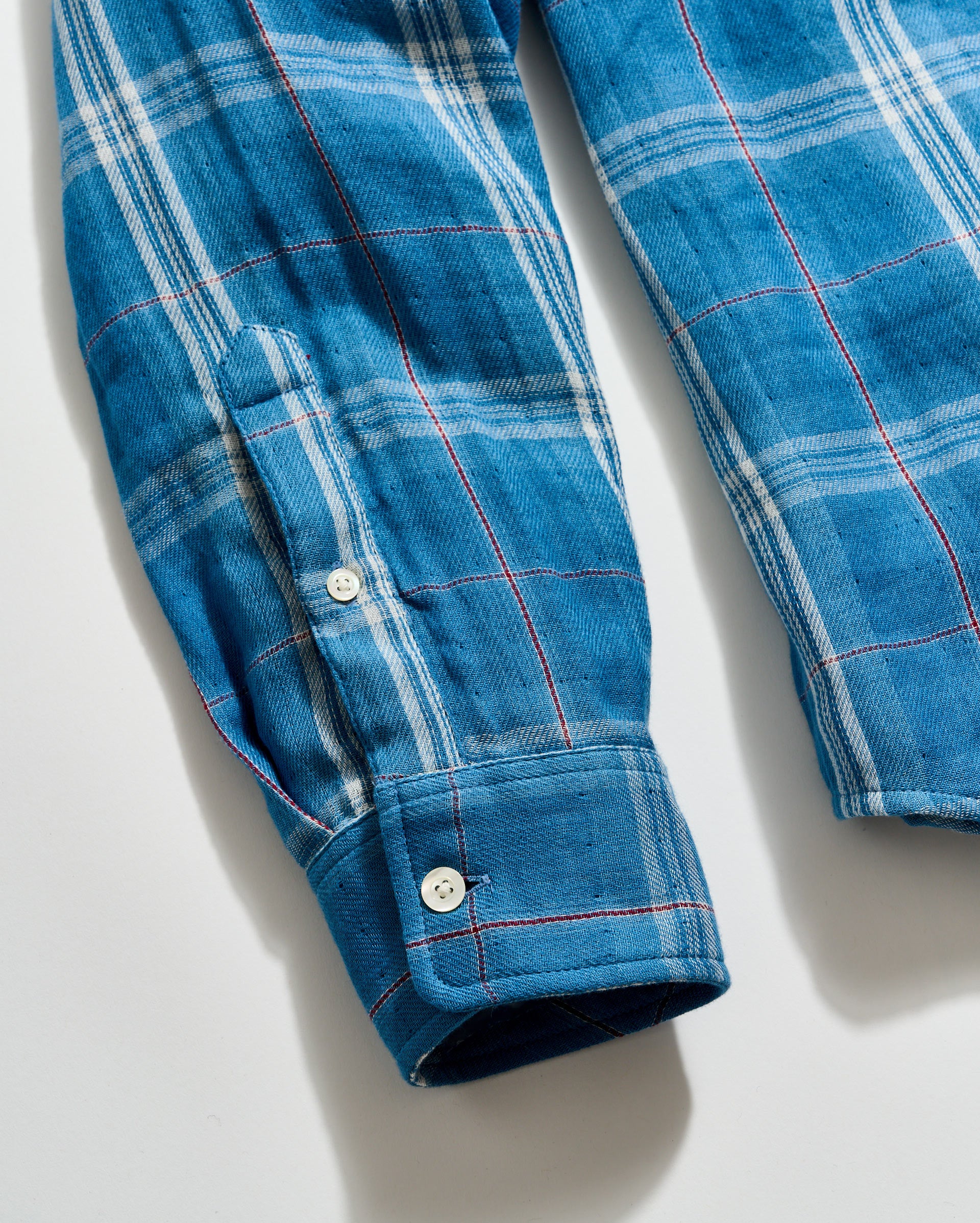 Close-up of a blue plaid shirt with rolled-up sleeves on a light background