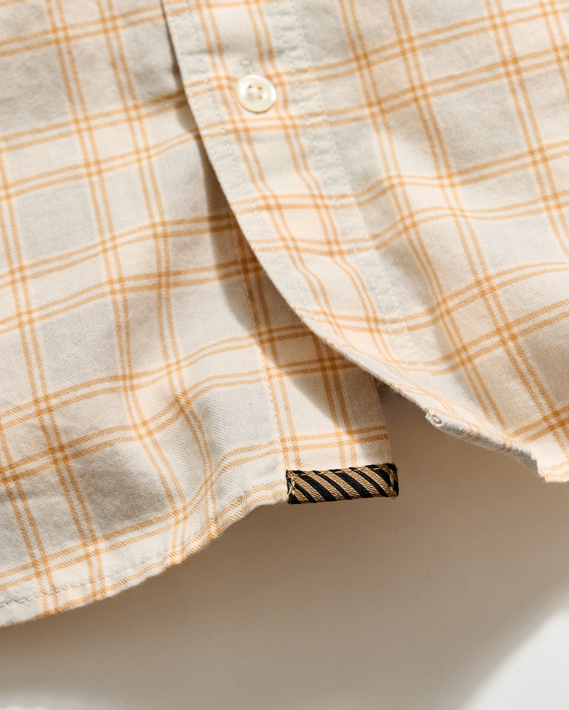 Close-up of a beige and orange plaid shirt with a brand label on a white background