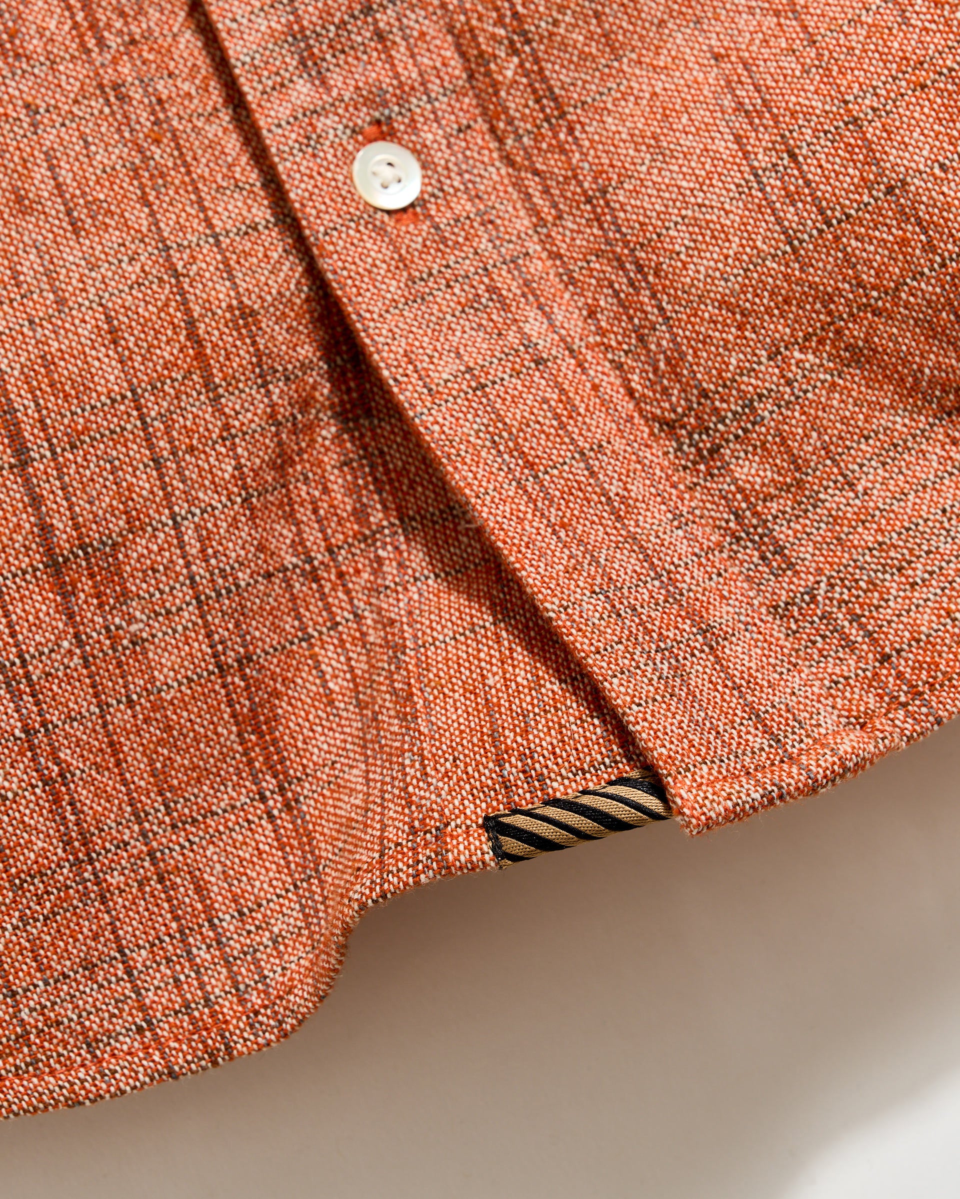 Close-up of a textured orange fabric with a button and striped trim.