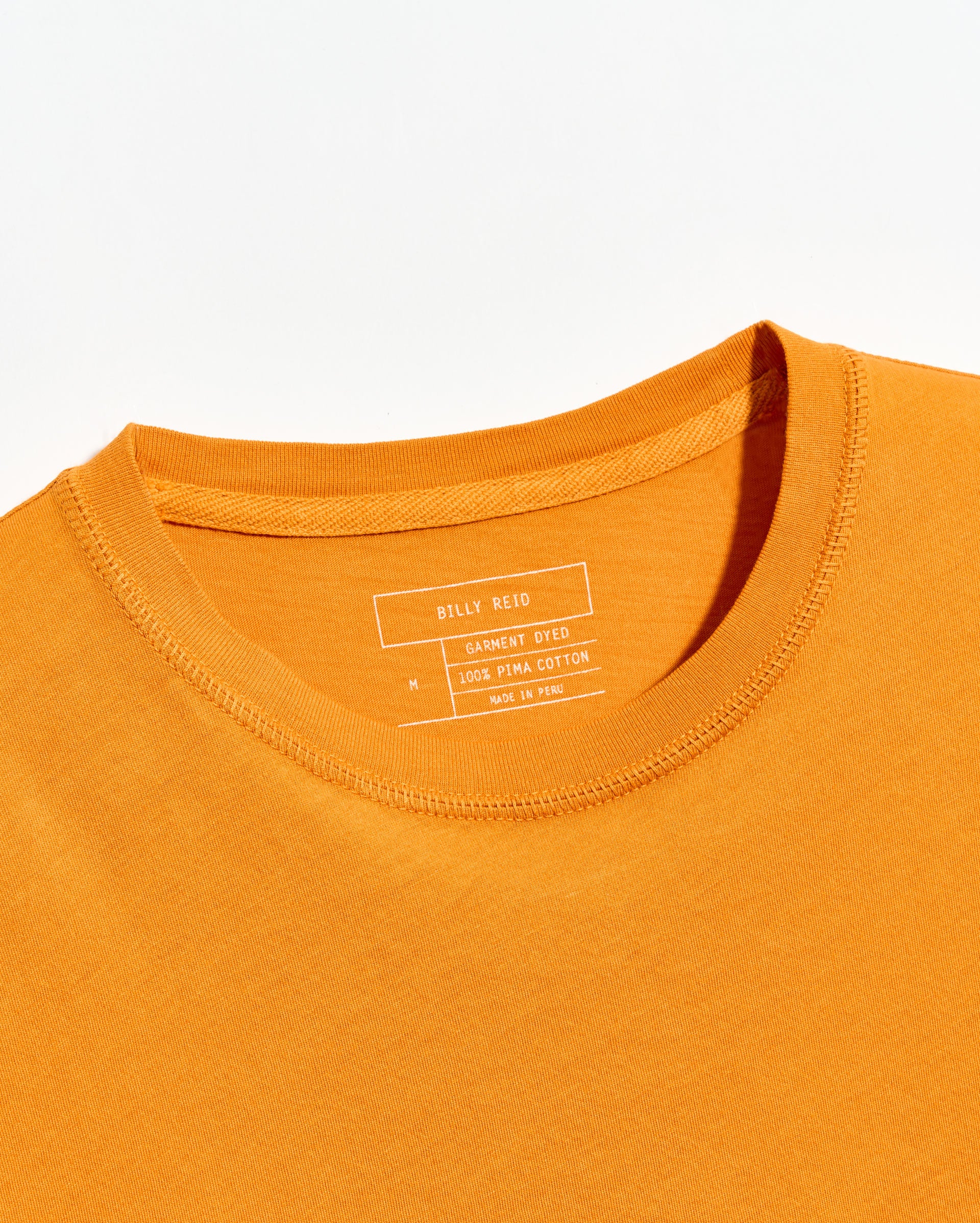 Close-up of an orange t-shirt with a brand label on a white background