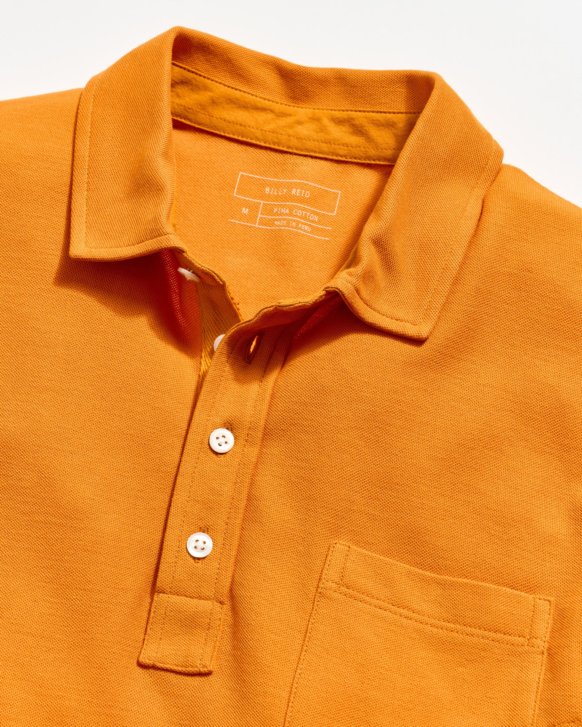 Close-up of an orange polo shirt with a brand label on a light gray background