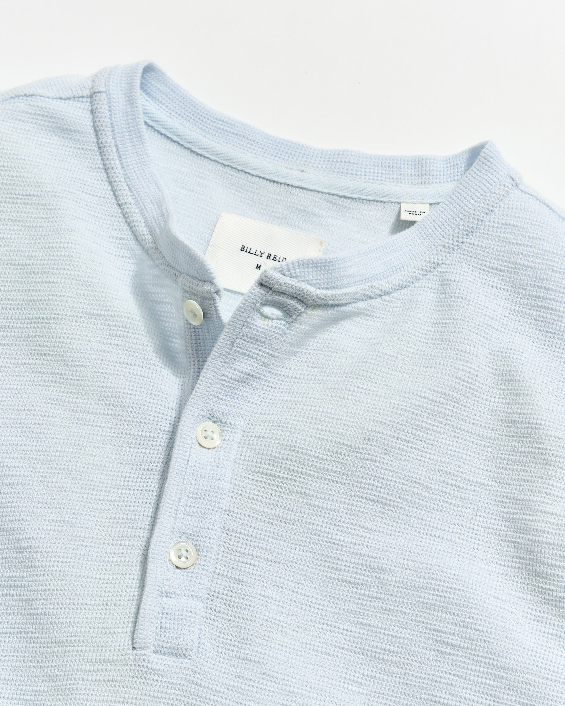 Light blue textured shirt with buttons and a visible brand tag on a light gray background