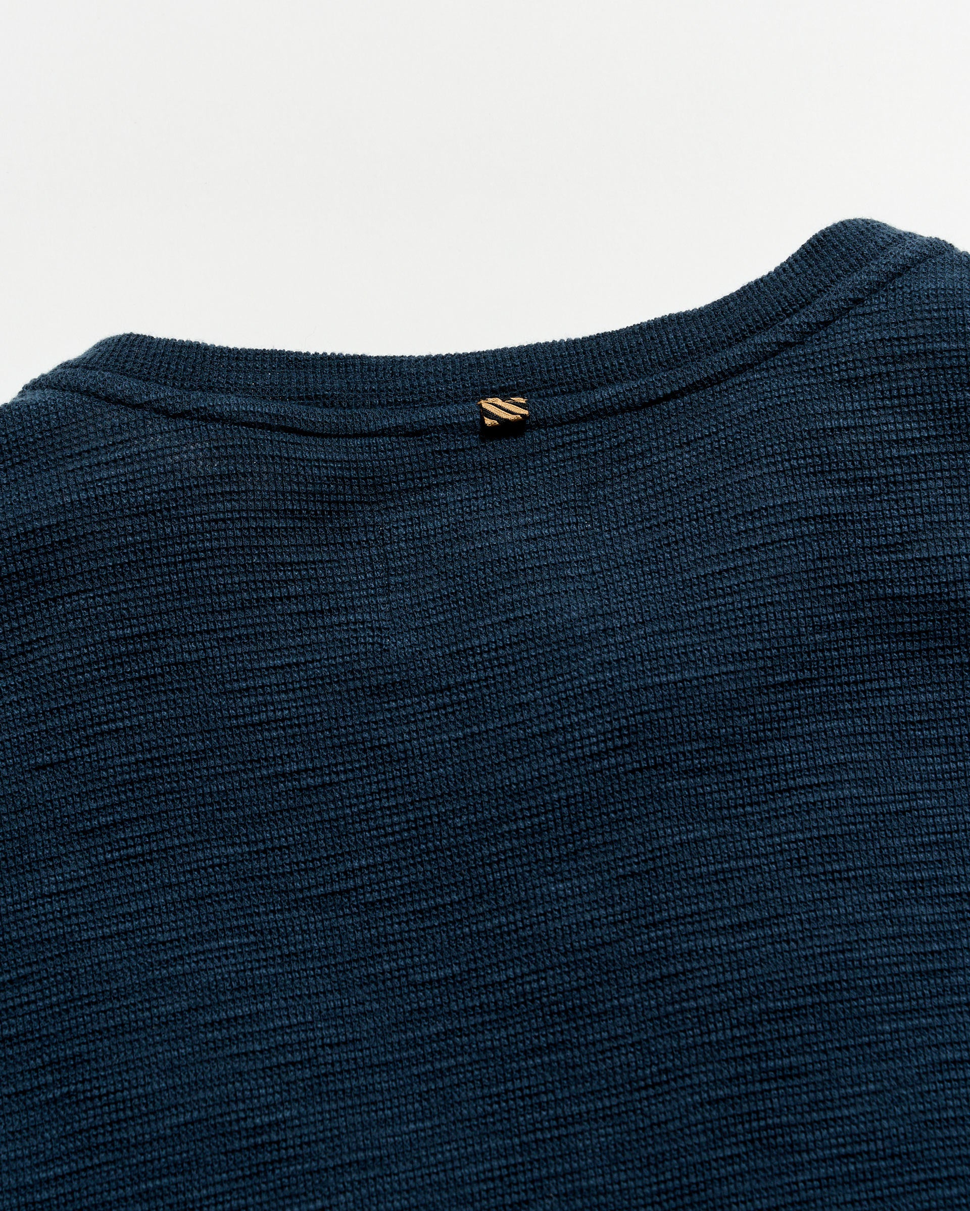 Close-up of a dark blue garment with a brand logo on a light gray background