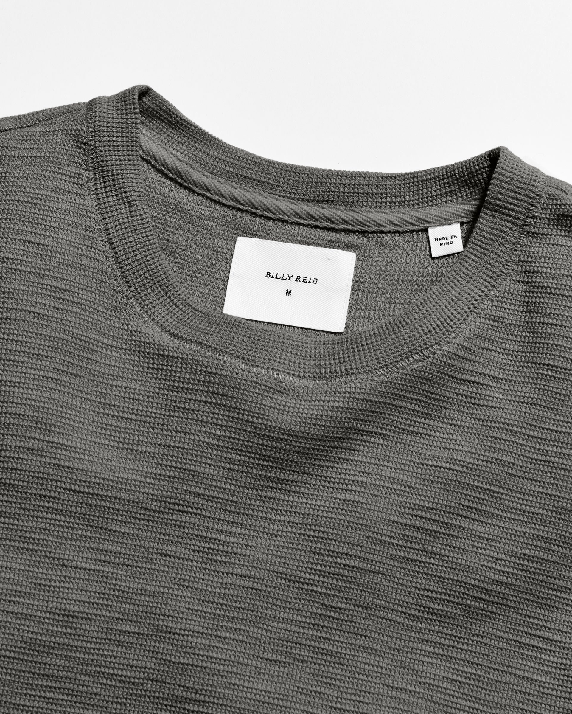 Close-up of a gray t-shirt with a brand label on a white background