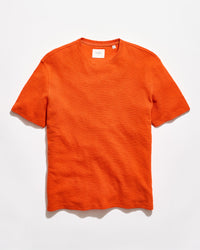 Orange crew neck shirt on a grey background.