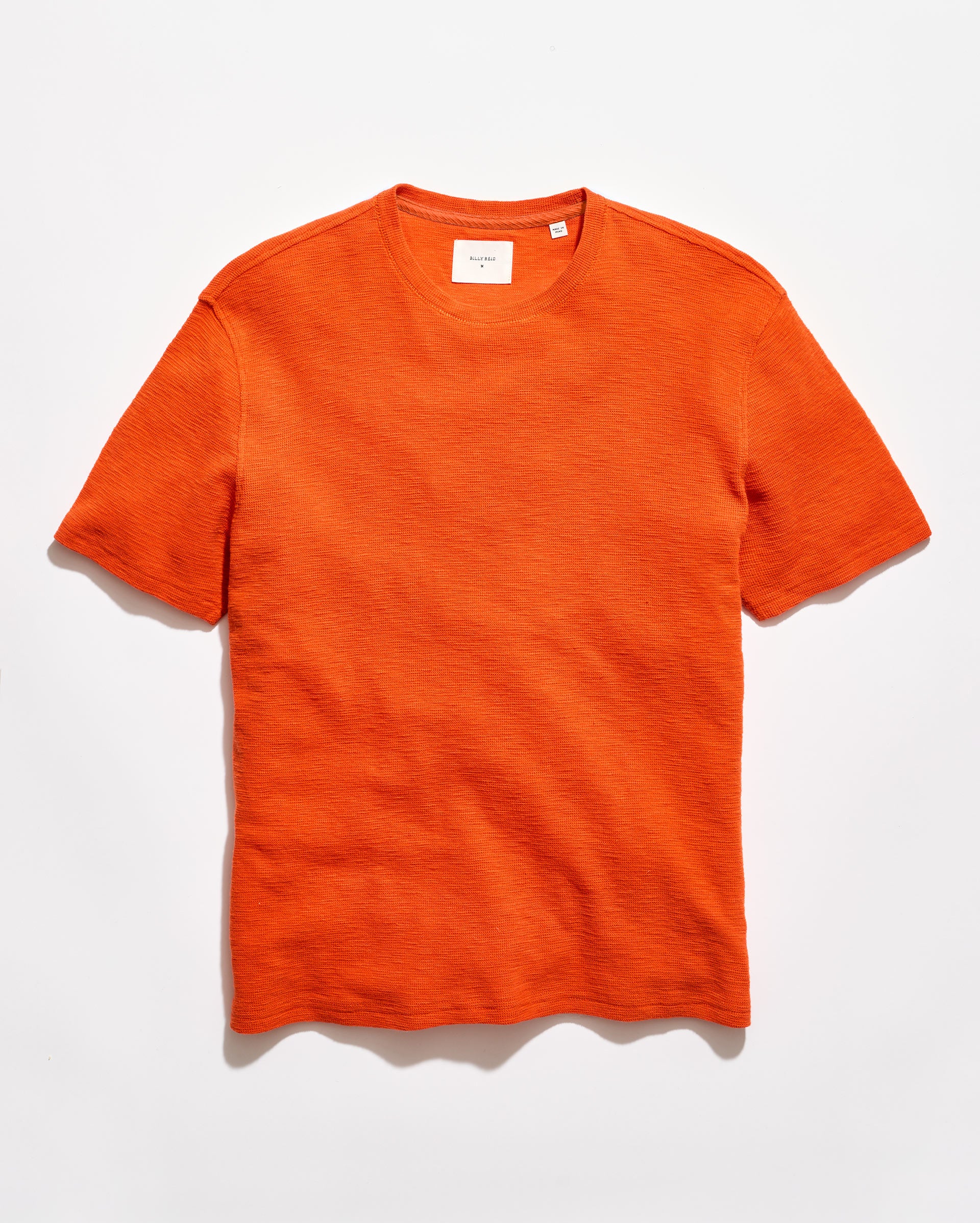 Orange crew neck shirt on a grey background.