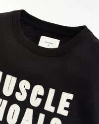 Black t-shirt with 'MUSCLE SHOALS' text and a visible brand label on a white background