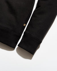 Close-up of a black sweatshirt with a brand logo on the sleeve against a white background