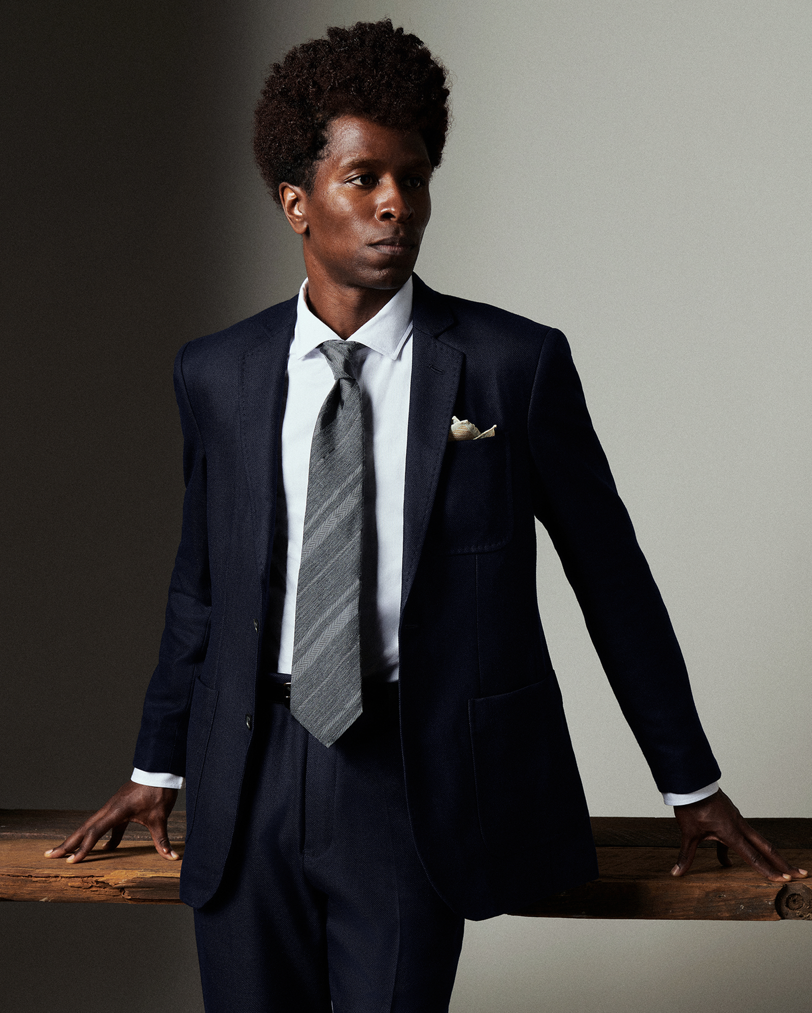 Man wearing a navy suit with a gray tie and pocket square against a neutral background