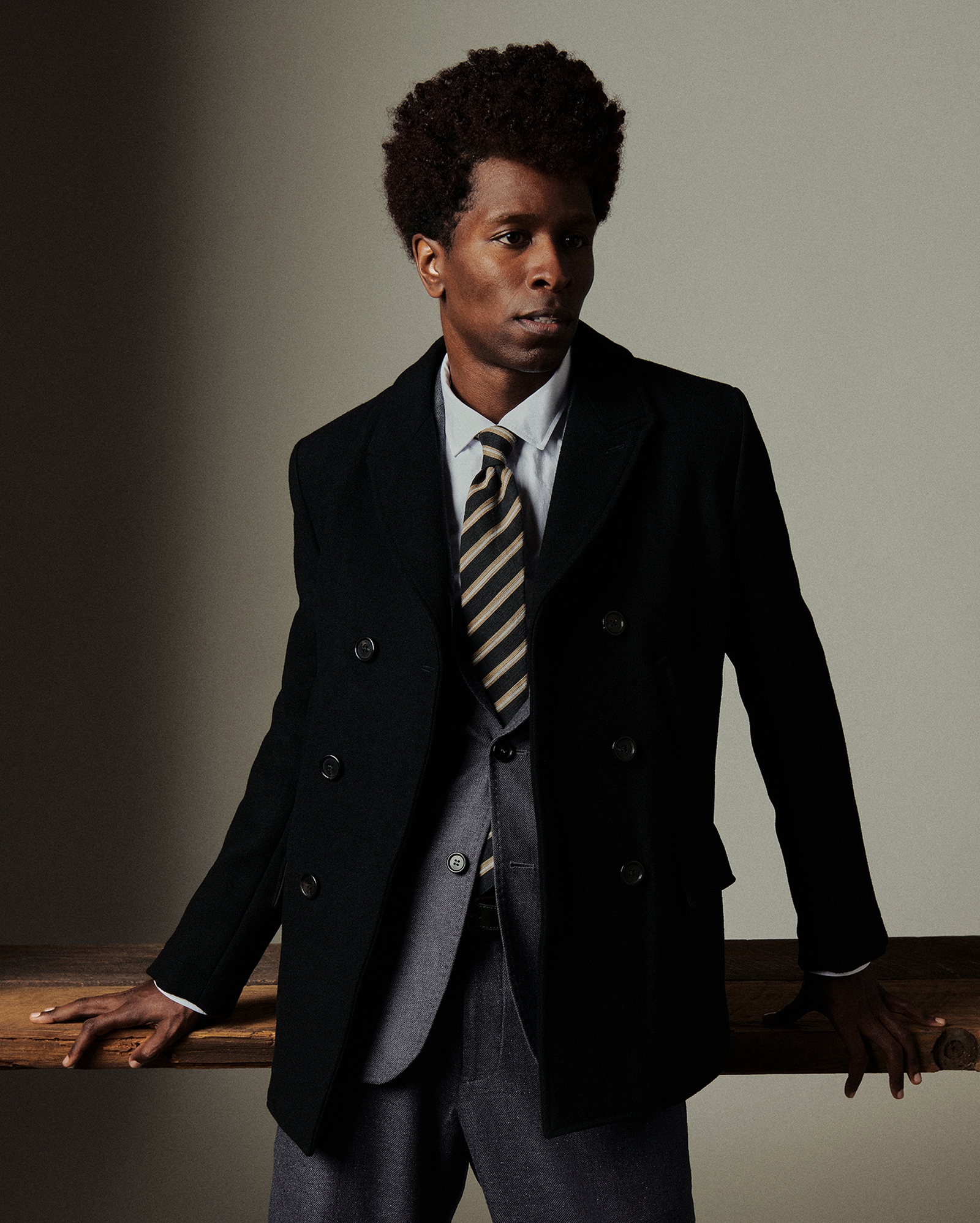 Man wearing a dark suit with a striped tie against a plain background