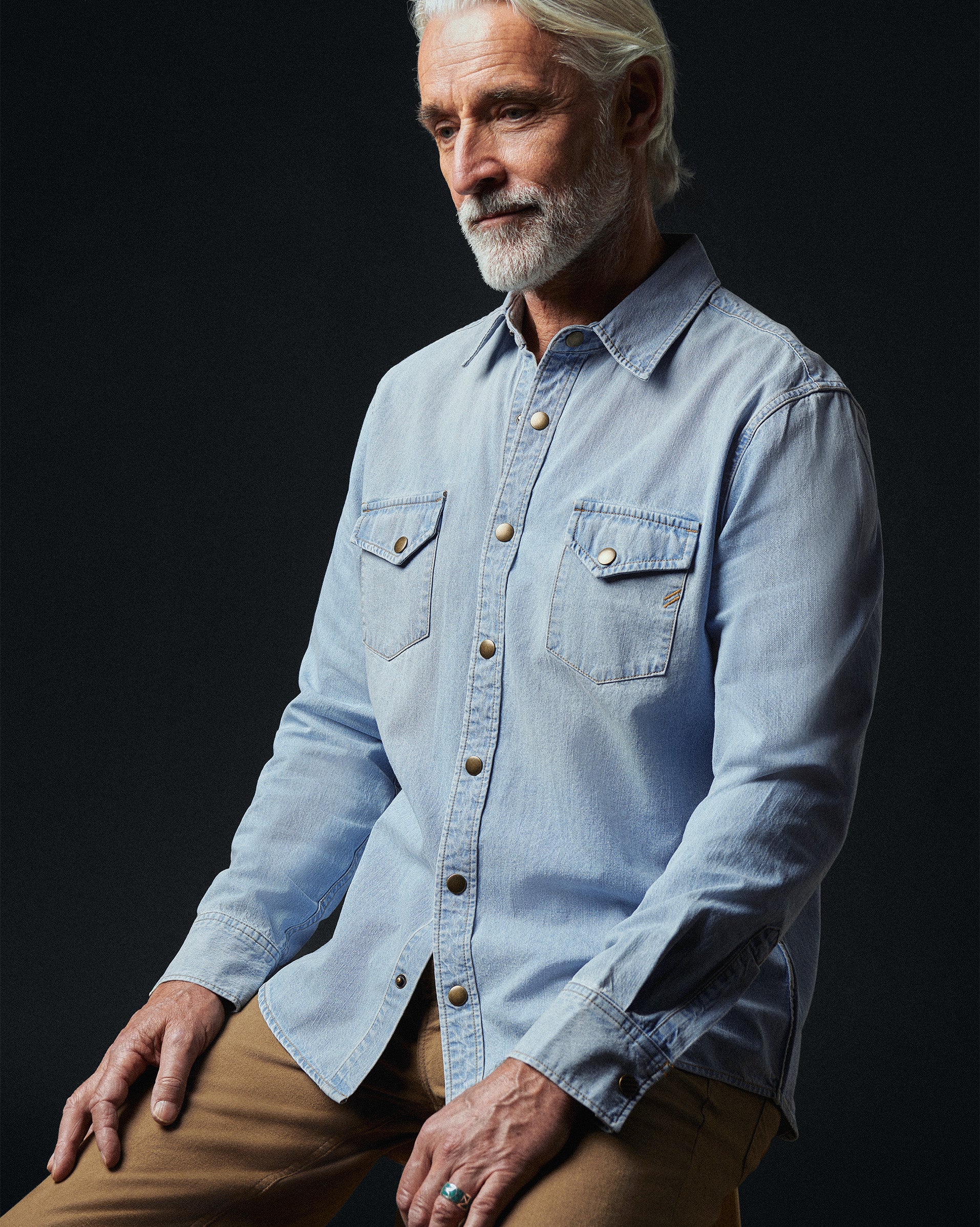 Man wearing a light blue denim shirt against a black background